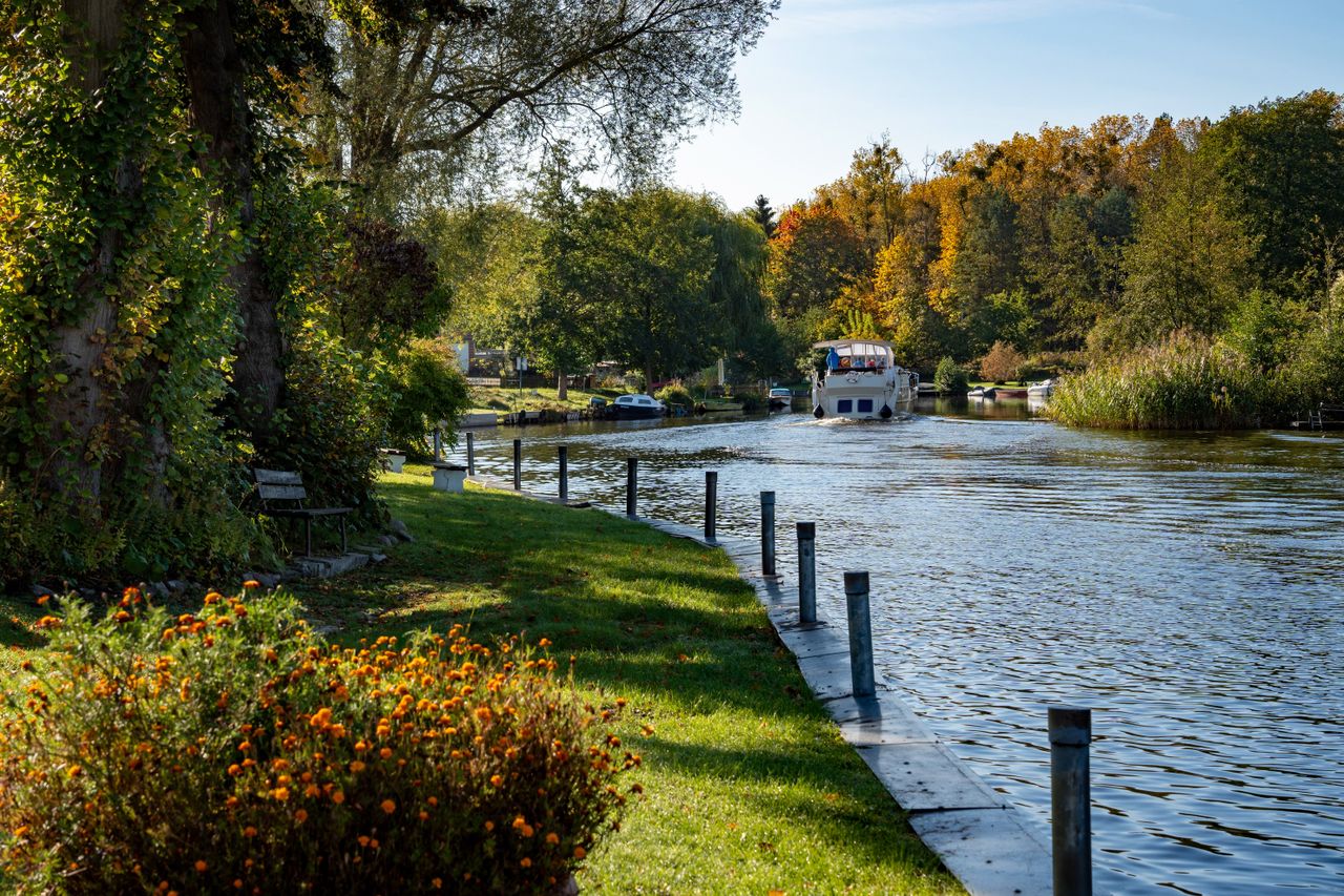 ours-journey Charming autumn scene of a peaceful canal with vibrant trees and a passing boat.
