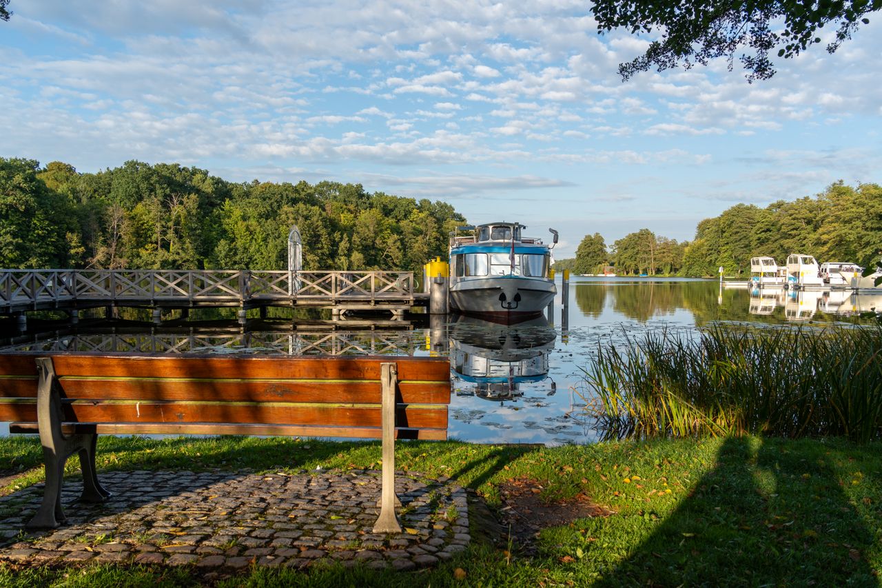 Peaceful lakeside scene featuring docked boats, a wooden walkway, and a cozy bench.